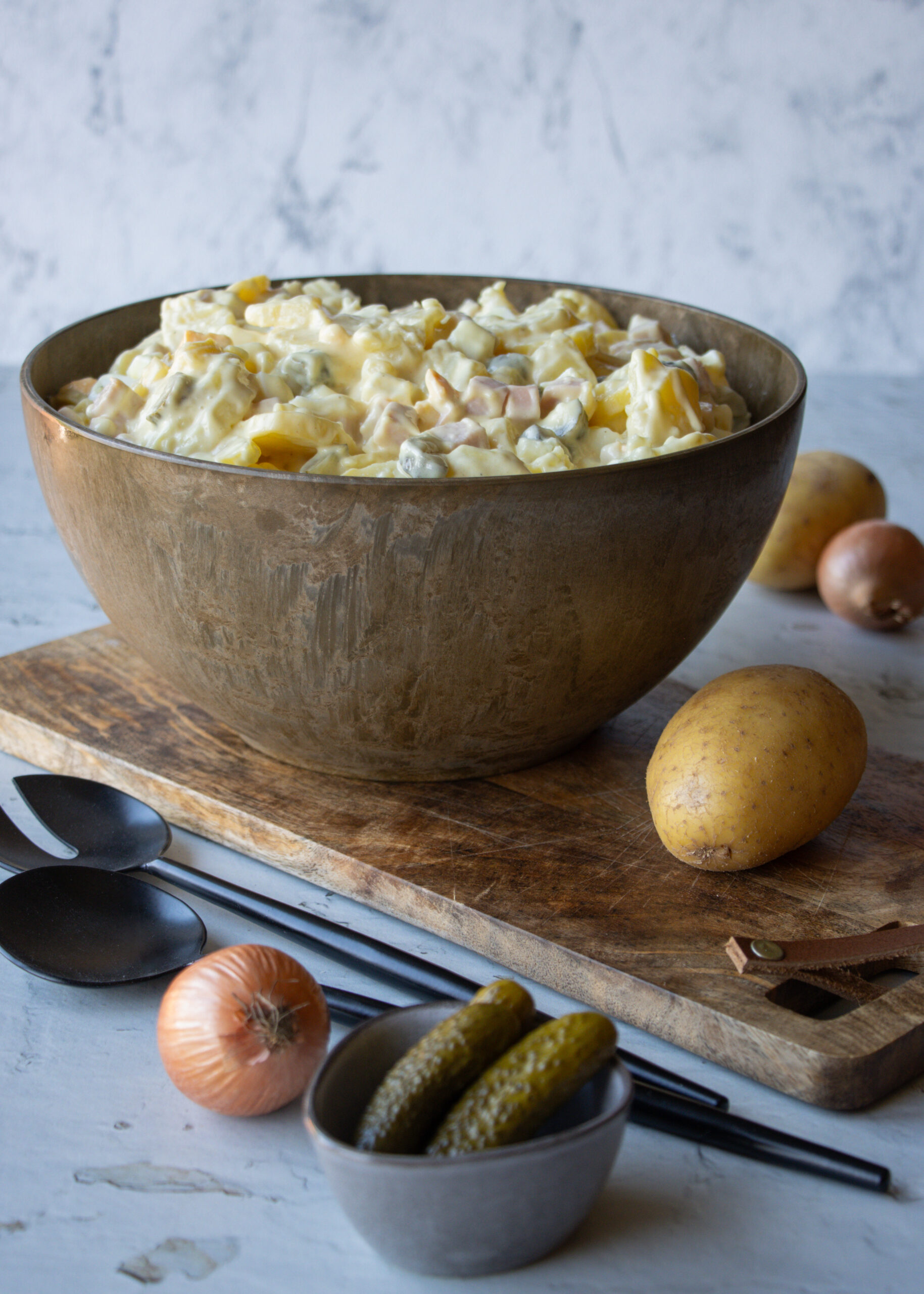 Kartoffelsalat mit Mayonnaise, Eiern, Gürkchen und Fleischwurst - in einer großen Schüssel serviert, drumherum einzelne Zutaten