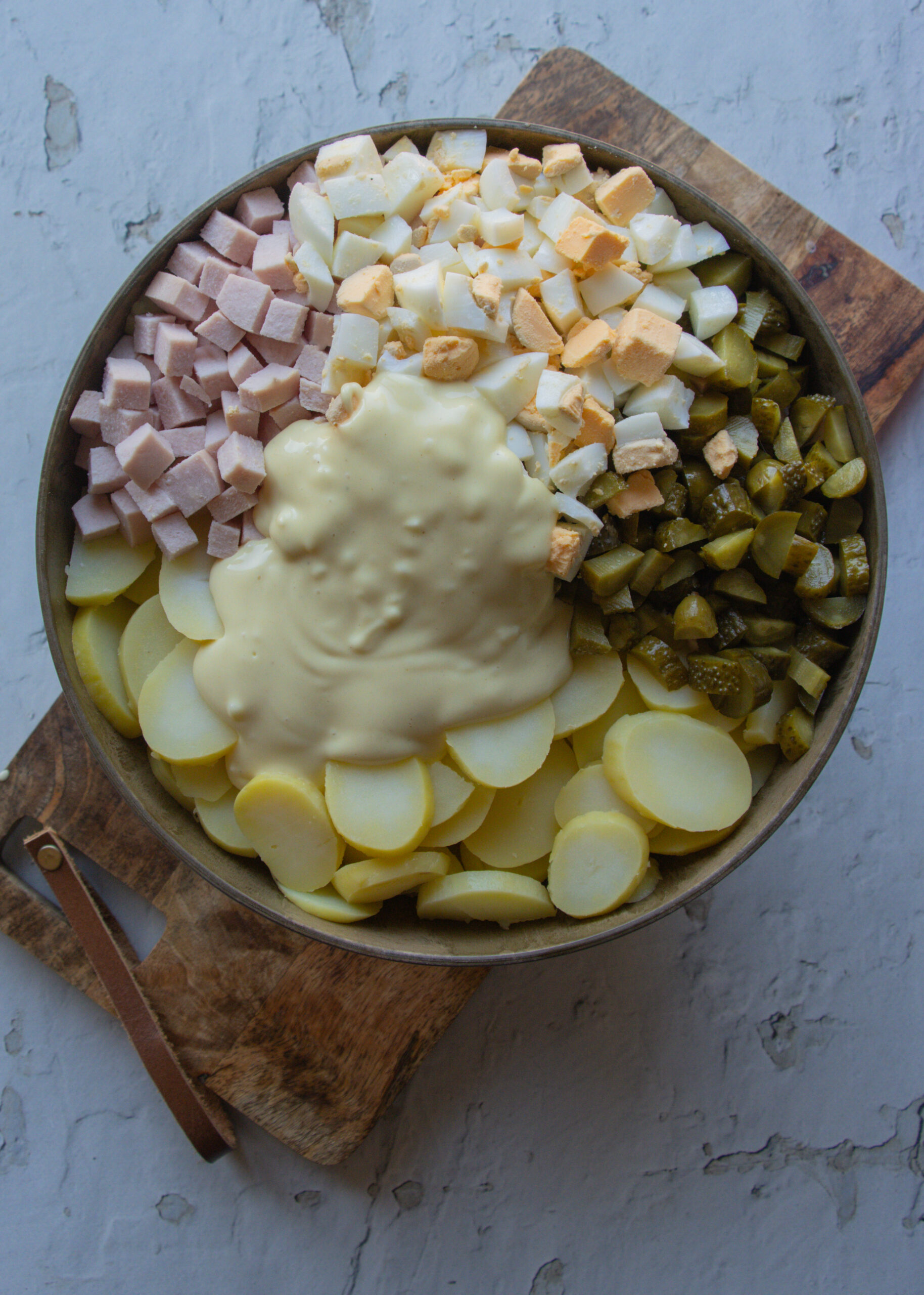 Zutaten für einen deftigen Kartoffelsalat in einer großen Schüssel serviert, ein Klecks Dressing in der Mitte